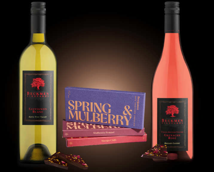 Two wine bottles, one white and one rose, with a three Spring & Mulberry chocolates on a dark background.