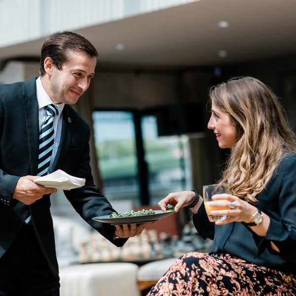 Man in a suit serving food to a woman in an outdoor setting